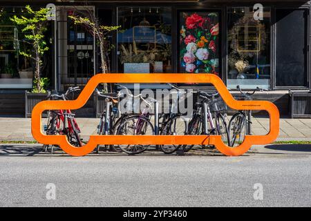 Un porte-vélos avec une façade orange en forme de silhouette de voiture fabriqué par Cyclehoop à Malmö, Suède, avec une dizaine de vélos verrouillés sur les barres. Banque D'Images