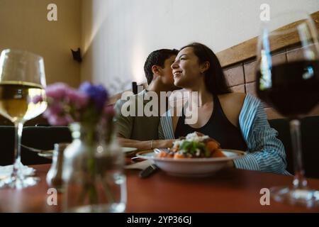 Homme chuchotant à l'oreille de la femme assis avec de la nourriture sur la table au restaurant Banque D'Images