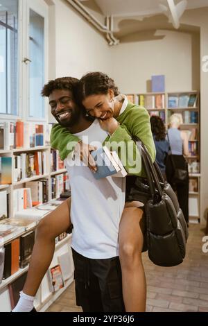 Souriant homme piggyback petite amie dans la librairie Banque D'Images