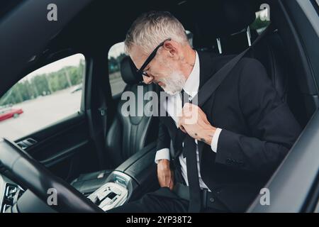 Homme d'affaires mature portant un costume sécurise la ceinture de sécurité dans une voiture au parking Banque D'Images