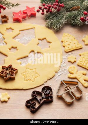 La pâte déroulée est en cours de préparation pour les biscuits de noël, avec diverses formes festives comme des maisons, des arbres, des étoiles et des flocons de neige Banque D'Images