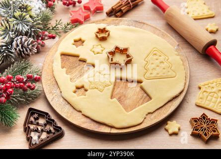 La pâte déroulée est en cours de préparation pour les biscuits de noël, avec diverses formes festives comme des maisons, des arbres, des étoiles et des flocons de neige Banque D'Images