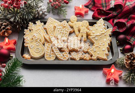 Plat de biscuits de pain d'épices de noël sur une plaque de cuisson, entouré de décorations festives et de bougies allumées, créant un SC de vacances chaleureux et accueillant Banque D'Images