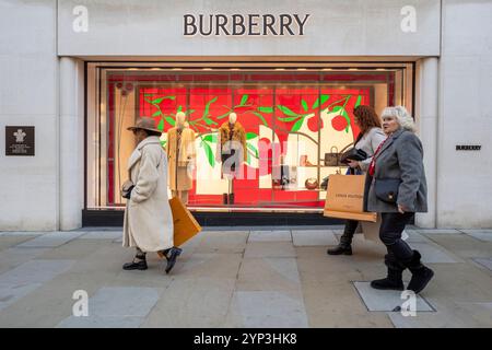 Londres, Royaume-Uni. 28 novembre 2024. Les acheteurs portant des sacs Louis Vuitton passent des décorations de Noël dans les vitrines du magasin Burberry de New Bond Street dans le West End. New Bond Street a récemment été élue troisième rue commerçante la plus chère au monde, la via Montenapoleone de Milan dépassant la Upper 5th Avenue de New York pour occuper la première place. Credit : Stephen Chung / Alamy Live News Banque D'Images