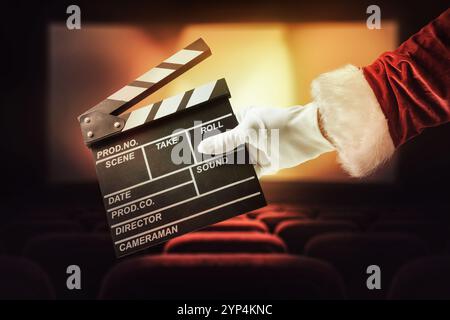 Concept de cinéma de vacances de Noël avec la main du Père Noël tenant un clapet dans une salle de cinéma avec des sièges rouges et un écran en arrière-plan Banque D'Images