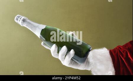 Père Noël main en costume et gants tenant une bouteille de vin mousseux sur fond vert isolé. Banque D'Images