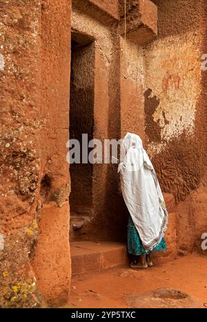 Femme orthodoxe éthiopienne priant à la porte de l'église taillée dans la roche Biete Gabriel-Rufael, site du patrimoine culturel mondial de l'UNESCO Lalibela, Ethiopie Banque D'Images