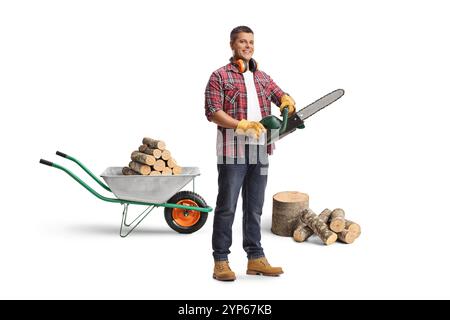 Portrait en pied d'un jeune homme avec des piles de bois de chauffage tenant une tronçonneuse isolée sur fond bleu Banque D'Images