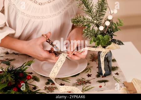 une fille dans une blouse blanche à volants sélectionne soigneusement les éléments pour décorer la table. Elle tient des ciseaux dans une main et du ruban adhésif dans l'autre. Banque D'Images