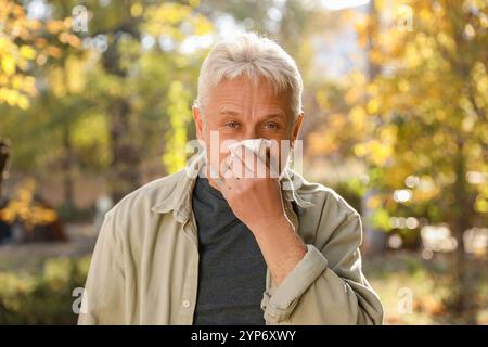 Homme senior avec des tissus soufflant le nez qui coule dans le parc Banque D'Images