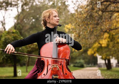 Belle jeune femme jouant au violoncelle dans le parc Banque D'Images