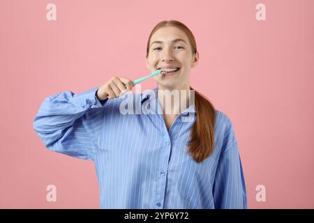 Fille avec des accolades nettoyant les dents sur fond rose Banque D'Images