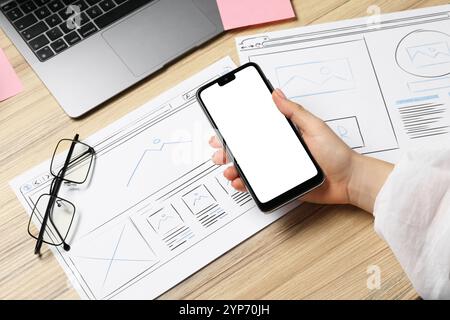 Concepteur de site Web tenant smartphone à la table en bois avec wireframes et ordinateur portable, gros plan Banque D'Images