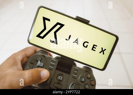 Dans cette illustration photo, une personne joue sur un joystick et le logo Jagex Limited est affiché sur un écran de smartphone Banque D'Images