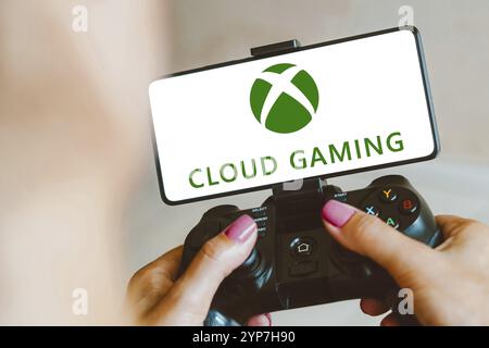 Dans cette illustration photo, le logo Xbox Cloud Gaming s'affiche sur l'écran d'un smartphone lorsqu'une personne joue sur une manette de jeu Banque D'Images