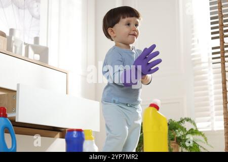 Petit garçon jouant avec un gant parmi les bouteilles de détergents près de l'armoire à la maison. Enfant en danger Banque D'Images