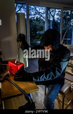 Image symbolique d'un cambriolage, l'auteur est entré par effraction dans un appartement du côté du jardin et est à la recherche de butin, ouvre une caisse, valuabl Banque D'Images