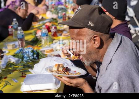 Los Angeles, États-Unis. 29 novembre 2024. Les gens apprécient leur repas de Thanksgiving. Des milliers de résidents de Skid Row et de sans-abri du centre-ville et au-delà ont été servis des dîners de Thanksgiving pendant la fête annuelle de la mission de Los Angeles. Crédit : SOPA images Limited/Alamy Live News Banque D'Images