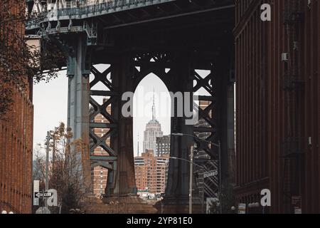 Une composition urbaine saisissante mettant en valeur l'Empire State Building parfaitement encadré par l'arche en acier complexe du pont de Manhattan à DUMBO, Brook Banque D'Images