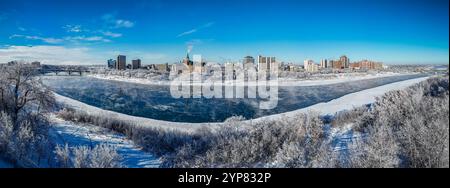 Une ligne d'horizon de la ville est visible au loin, avec une rivière qui la traverse. Le ciel est clair et bleu, et les arbres enneigés ajoutent un sentiment de calme Banque D'Images