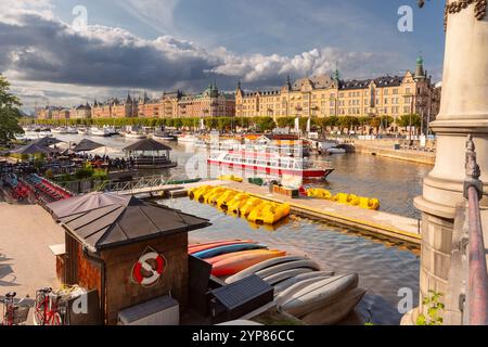 Le port de Nybroviken à Stockholm avec des kayaks colorés, des bateaux amarrés et un bateau d'excursion rouge sur l'eau, Suède, Banque D'Images