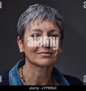 Portrait studio d'une belle femme mature souriante aux cheveux gris et boucles d'oreilles en perles, portant une veste en denim et un pull noir, regardant le venu Banque D'Images