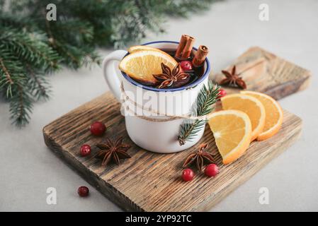 Tasse avec boisson chaude, vin chaud avec tranches d'orange, bâtonnets de canneberge et cannelle sur planche à découper en bois et branches de sapin sur fond Banque D'Images