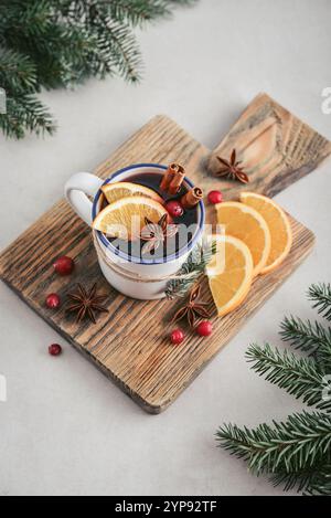 Tasse avec boisson chaude, vin chaud avec tranches d'orange, bâtonnets de canneberge et cannelle sur planche à découper en bois et branches de sapin sur fond Banque D'Images