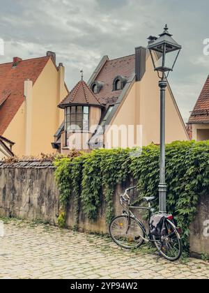 Vélo noir sous un buisson près d'une clôture en pierre près d'une vieille maison avec un toit de tuiles rouges dans la vieille ville de Nuremberg Banque D'Images