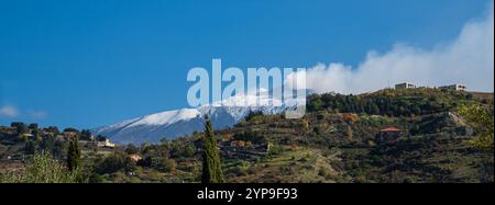 Paysage d'hiver panoramique montrant l'Etna avec la neige et la vapeur de l'activité volcanique, vu de Bronte colline avec des maisons rurales typiques et moi Banque D'Images