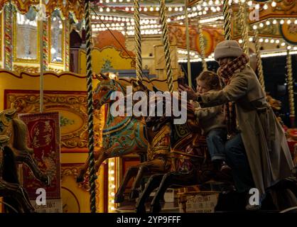 Enfant et parent profitent d'une balade magique sur un carrousel illuminé lors d'une fête nocturne festive du marché de Noël de York 2024 Banque D'Images