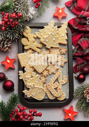 Plat de biscuits de pain d'épices de noël sur une plaque de cuisson, entouré de décorations festives et de bougies allumées, créant un SC de vacances chaleureux et accueillant Banque D'Images