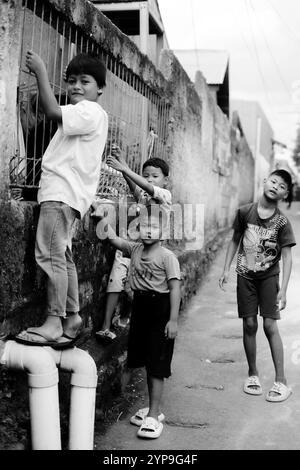 Bogor, 24 novembre 2024. Quatre jeunes enfants debout ensemble dans une ruelle étroite, souriant et regardant autour dans un cadre de quartier animé Banque D'Images