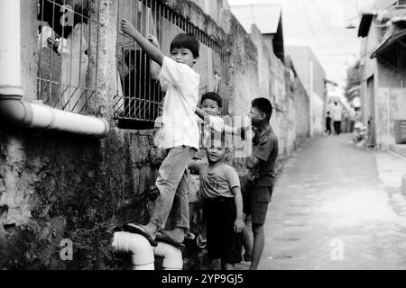 Bogor, 24 novembre 2024. Quatre jeunes enfants debout ensemble dans une ruelle étroite, souriant et regardant autour dans un cadre de quartier animé Banque D'Images