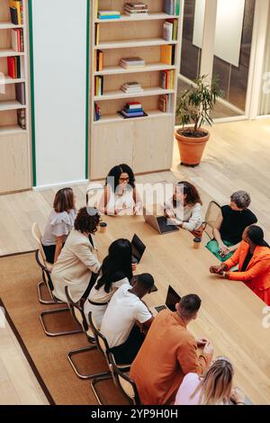 Une photo aérienne capture un groupe coloré de professionnels dans un bureau moderne, réunis autour d'une grande table, discutant d'idées et travaillant ensemble Banque D'Images