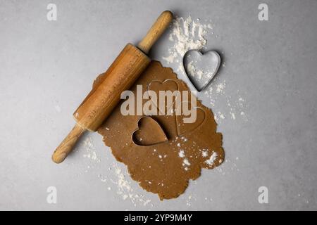 Préparer des biscuits en forme de coeur avec rouleau à pâtisserie et emporte-pièce sur une surface farinée dans une ambiance de cuisine chaleureuse. Banque D'Images