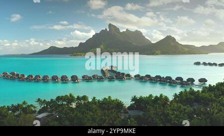 Vue aérienne à couper le souffle sur le lagon turquoise, plage de palmiers, bungalows sur l'eau Resort sur l'île tropicale de Bora Bora. Lumière verte du coucher de soleil de montagne. Destination touristique populaire, voyage d'été exotique Banque D'Images