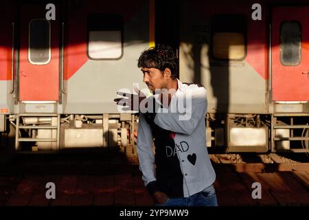 Un jeune homme indien à la gare de Dadar à Mumbai, Inde, gesticulant, avec un train en arrière-plan Banque D'Images