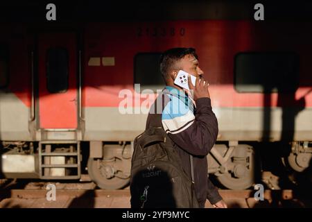 Un jeune Indien à la gare de Dadar à Mumbai, en Inde, parlant sur son téléphone portable, avec un train en arrière-plan Banque D'Images