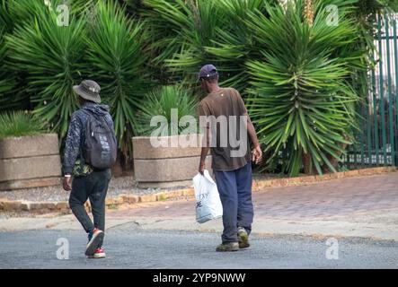 Johannesburg, Afrique du Sud - deux chômeurs noirs non identifiés rentrent chez eux après un travail à la pièce dans un quartier résidentiel Banque D'Images