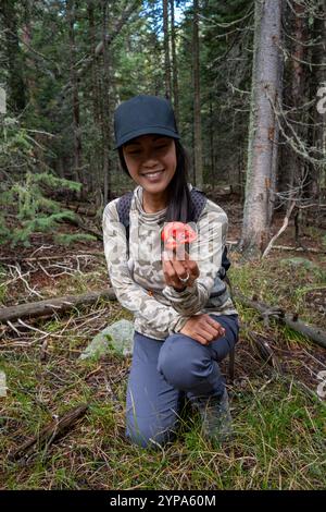 Une femme sourit en cherchant des champignons dans la forêt. Banque D'Images