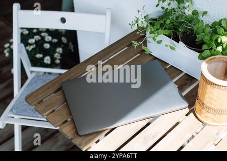 Ordinateur portable fermé sur table en bois extérieure avec plantes et chaise à proximité Banque D'Images