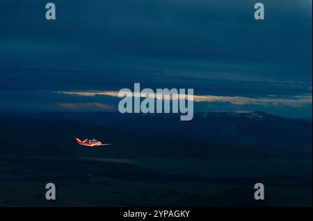 Un petit avion vole contre une chaîne de montagnes au coucher du soleil. Banque D'Images