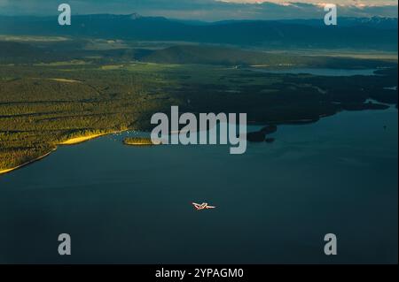 Un petit avion survole un lac au coucher du soleil. Banque D'Images
