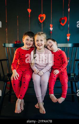 Trois enfants souriants en pyjama assis sur un banc noir Banque D'Images