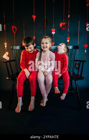 Trois enfants joyeux en pyjama avec des décorations coeur de Saint-Valentin Banque D'Images