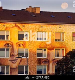 Mur d'un immeuble d'appartements peint avec des visages à la lumière du soir, art de rue, avec pleine lune, Allemagne, Rhénanie du Nord-Westphalie, Rhin inférieur, Dusse Banque D'Images