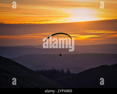 Un parapente monte au-dessus des collines et des vallées du Peak District avec le meilleur siège dans la maison pour profiter du soleil couchant. Banque D'Images