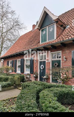 Ancienne maison allemande avec décoration de Noël à Neuenhaus, avec volets roulants, haies et neige sur tuiles rouges. Banque D'Images