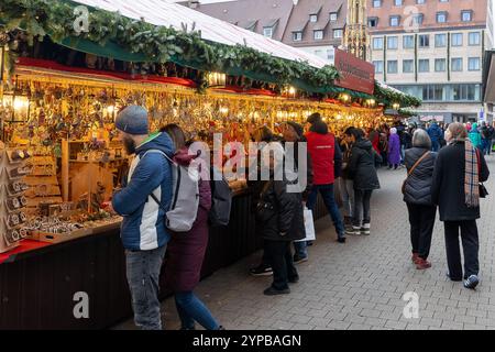 Eröffnungstag des Nürnberger Christkindlesmarkts 2024, 29.11.2024 Besucher betrachten und kaufen handgefertigte Weihnachtsdekorationen an einem festlich beleuchteten stand auf dem Nürnberger Christkindlesmarkt 2024. Der Verkaufsstand ist mit Tannengirlanden geschmückt und bietet eine große Auswahl an Krippenfiguren und weihnachtlichem Schmuck. Nürnberg Bayern Deutschland *** jour d'ouverture du Nuremberg Christkindlesmarkt 2024, 29 11 2024 les visiteurs regardent et achètent des décorations de Noël faites à la main dans un stand de Noël illuminé de façon festive au Nuremberg Christkindlesmarkt 2024 le stand est décoré de garlan de sapin Banque D'Images